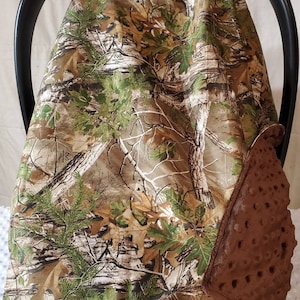 May include: Camouflage car seat cover with a brown padded insert. The cover is made of a soft, comfortable fabric and features a woodland camo pattern.