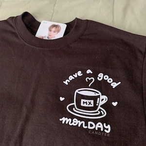 May include: A black t-shirt with a white graphic of a coffee cup with the text "have a good monday" and "MX" on the cup. The text "CANDTEE" is printed below the graphic.