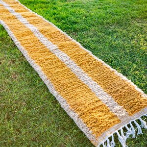 May include: A long, rectangular rug with a yellow and white striped pattern. The rug has a fringe on the ends and is made of a soft, fluffy material.