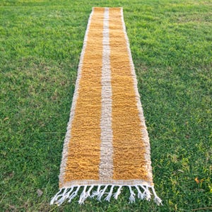 May include: A long, narrow, mustard yellow rug with two white stripes running down the centre. The rug has a fringe on both ends.