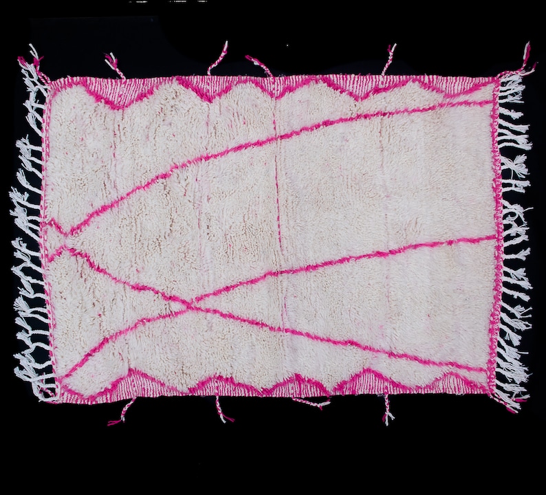 May include: White rug with a pink geometric design. The rug has a fringe border.