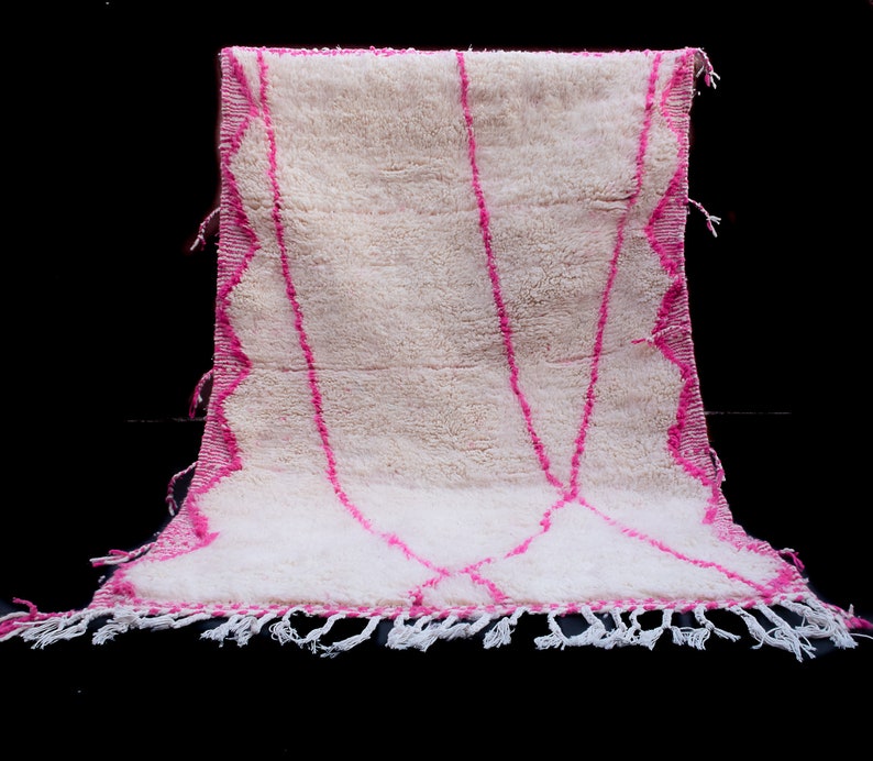 May include: White Moroccan rug with pink geometric designs and fringe.