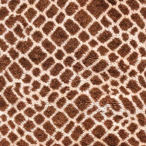 Puede incluir: Primer plano de un textil estampado marr&oacute;n y crema. El dise&ntilde;o presenta una cuadr&iacute;cula repetida de cuadrados y rect&aacute;ngulos marrones, delineados por l&iacute;neas color crema. La textura parece suave y afelpada, sugiriendo una tela como una alfombra o una manta.