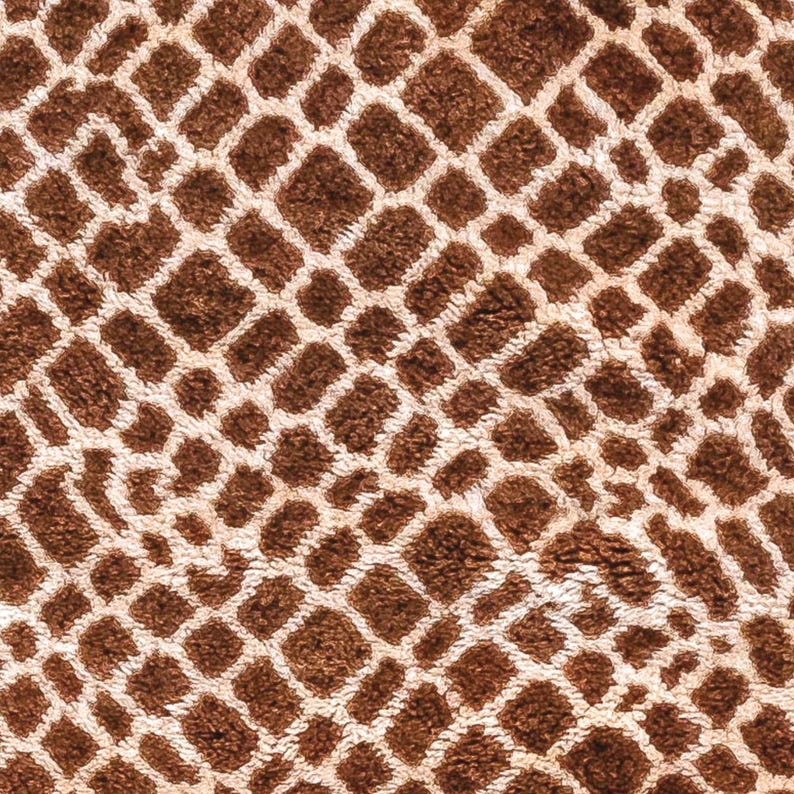 Puede incluir: Primer plano de un textil estampado marr&oacute;n y crema. El dise&ntilde;o presenta una cuadr&iacute;cula repetida de cuadrados y rect&aacute;ngulos marrones, delineados por l&iacute;neas color crema. La textura parece suave y afelpada, sugiriendo una tela como una alfombra o una manta.
