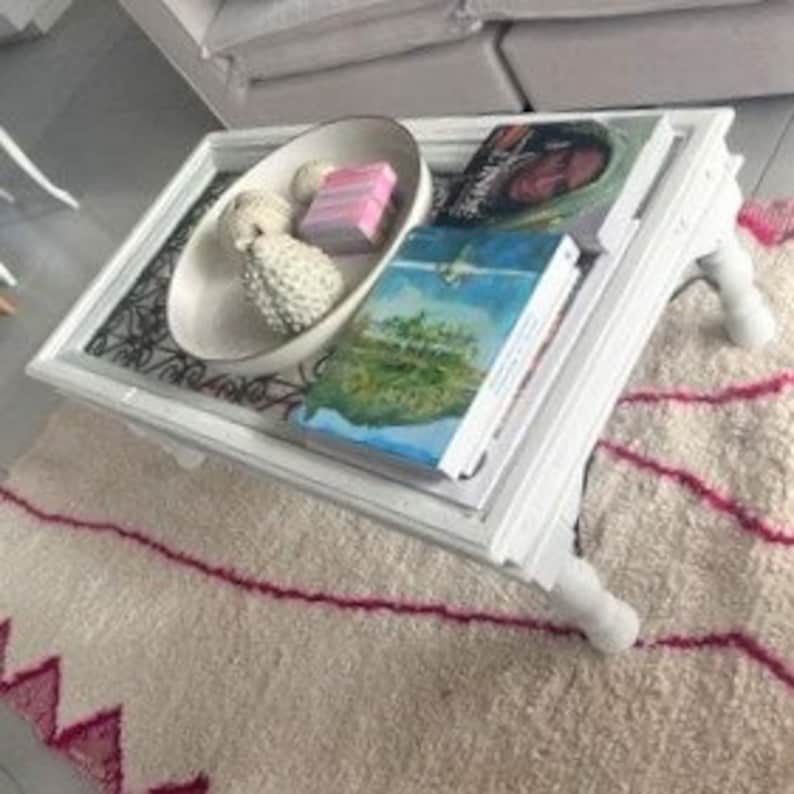 May include: White coffee table with a glass top and a decorative metal design. The table has four legs and is sitting on a white and pink rug.