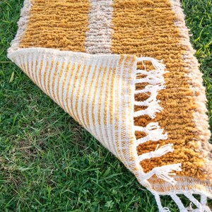 May include: A mustard yellow and white striped rug with fringe. The rug is folded in half and the fringe is visible on the bottom edge.
