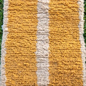 May include: A striped rug with a mustard yellow and off-white colour scheme. The rug has a fluffy, textured surface.
