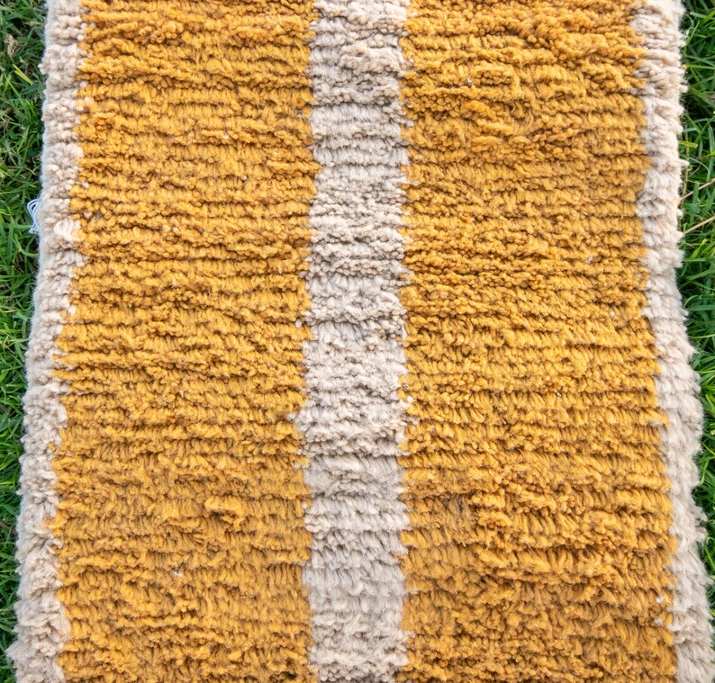 May include: A striped rug with a mustard yellow and off-white colour scheme. The rug has a fluffy, textured surface.