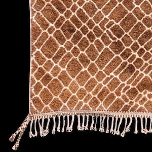 Puede incluir: Una alfombra estampada marr&oacute;n y blanca con dise&ntilde;o de estampado de jirafa. La alfombra tiene un patr&oacute;n de diamantes con un borde blanco. El borde inferior presenta flecos blancos. La alfombra est&aacute; hecha de un material suave y afelpado.