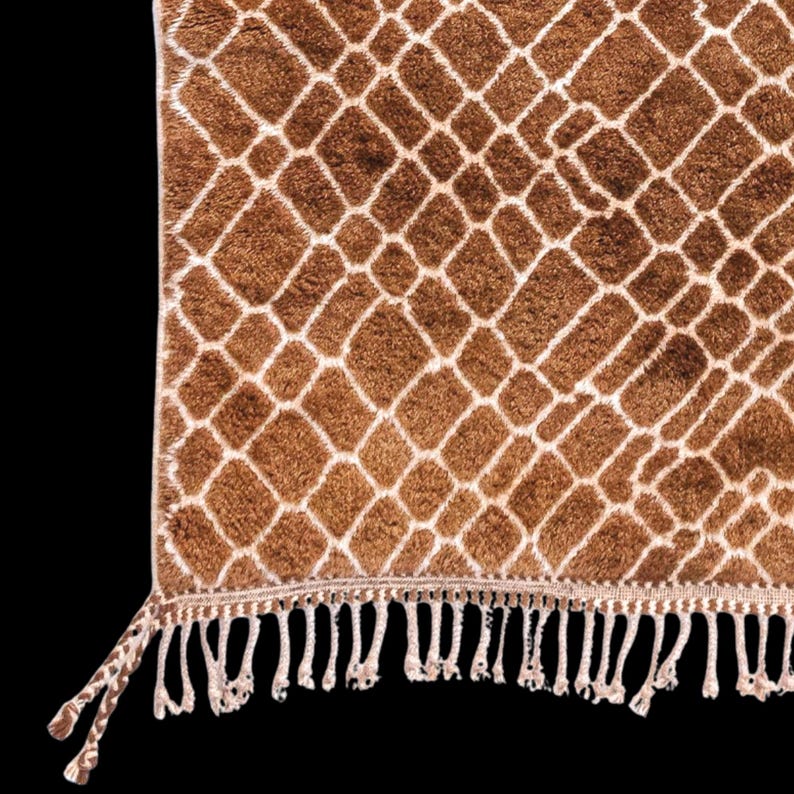 Puede incluir: Una alfombra estampada marr&oacute;n y blanca con dise&ntilde;o de estampado de jirafa. La alfombra tiene un patr&oacute;n de diamantes con un borde blanco. El borde inferior presenta flecos blancos. La alfombra est&aacute; hecha de un material suave y afelpado.
