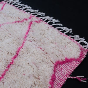 May include: White and pink Moroccan rug with a fluffy texture and fringe on the edges.