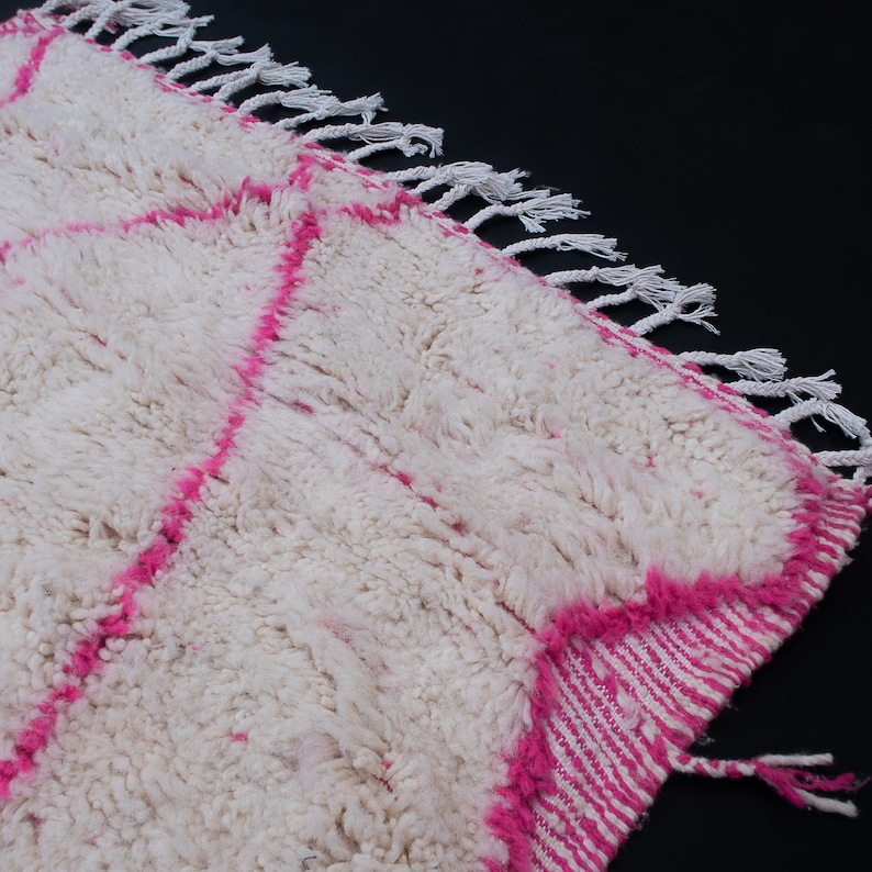 May include: White and pink Moroccan rug with a fluffy texture and fringe on the edges.