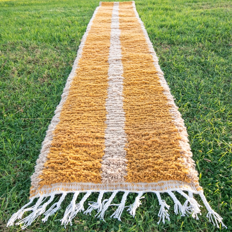 May include: A long, narrow, mustard yellow rug with a white stripe down the centre. The rug has a fringe on both ends.