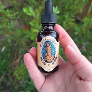 May include: A small, brown glass bottle with a black dropper. The label reads "My Sister's Apothecary" and features a mermaid illustration. The bottle contains "Rose Elixir" and is 1 oz.