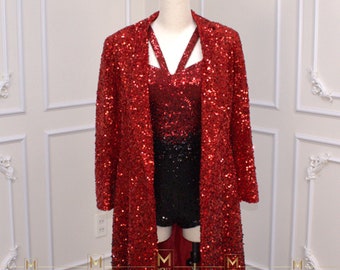 Puede incluir: Un conjunto de abrigo largo rojo con lentejuelas y un conjunto de top y shorts a juego. El abrigo largo es largo y abierto, con cuello. El top tiene un diseño de tirantes único. Los shorts son negros. El conjunto se exhibe en un maniquí.
