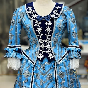 May include: A blue and white dress with a floral pattern and black trim. The dress has a fitted bodice with a velvet collar and a full skirt. The dress is decorated with white flowers and stars.