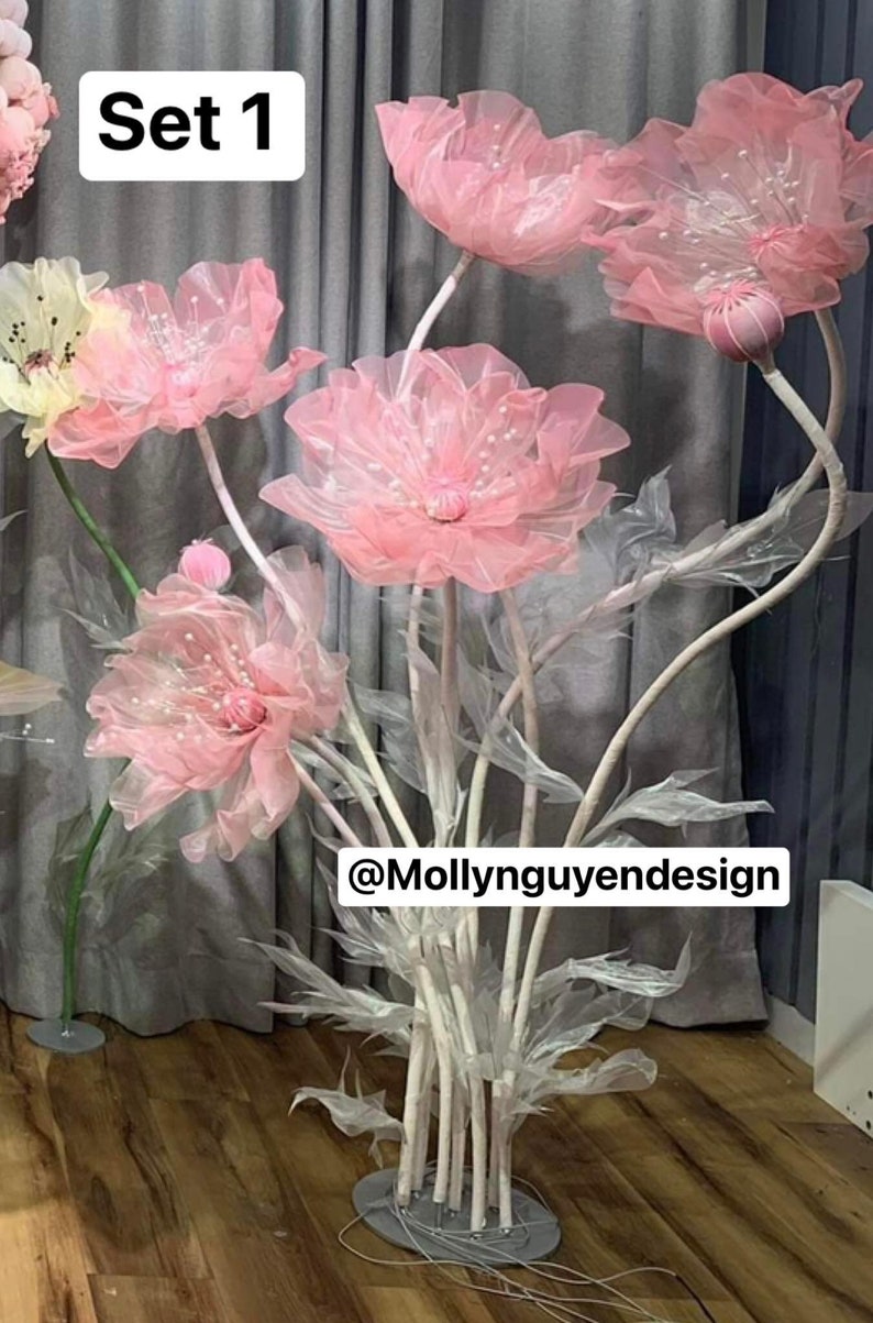 May include: Set of pink fabric flowers on white stems with a gray base. The flowers are made of sheer fabric and have a delicate, airy look. The text "Set 1" and "@Mollynguyendesign" are visible in the image.