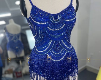 May include: A blue beaded top with fringe detailing. The top has a scoop neckline and spaghetti straps. The beads are arranged in a geometric pattern.