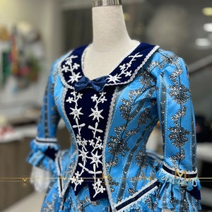 May include: A blue and white dress with a navy blue velvet bodice and white lace trim. The dress has a floral pattern and a star-shaped design on the bodice.