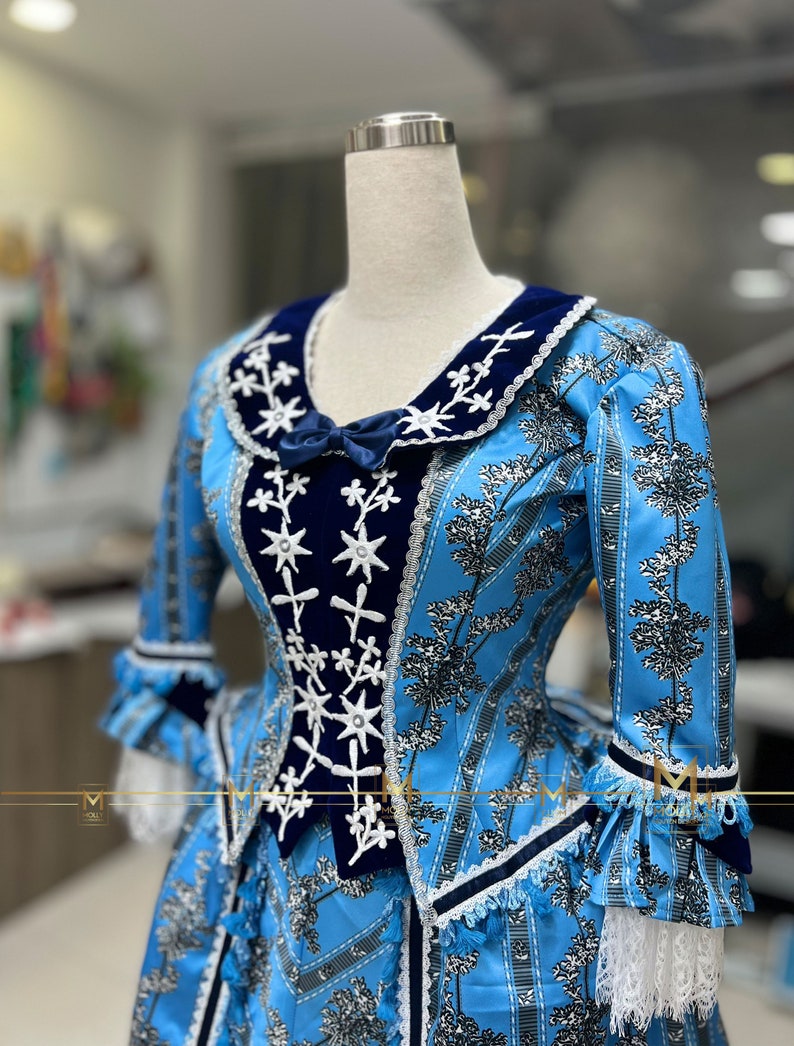 May include: A blue and white dress with a navy blue velvet bodice and white lace trim. The dress has a floral pattern and a star-shaped design on the bodice.