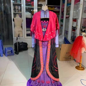 May include: A purple and black dress with a red cape and embroidered details. The dress has a long skirt with a purple trim and a black bodice with a gold belt. The cape is made of a soft, velvet-like fabric and has a fringe trim.