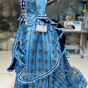 May include: A blue and white patterned dress with a ruffled skirt and a fitted bodice. The dress has a white lace trim and a blue velvet sash.