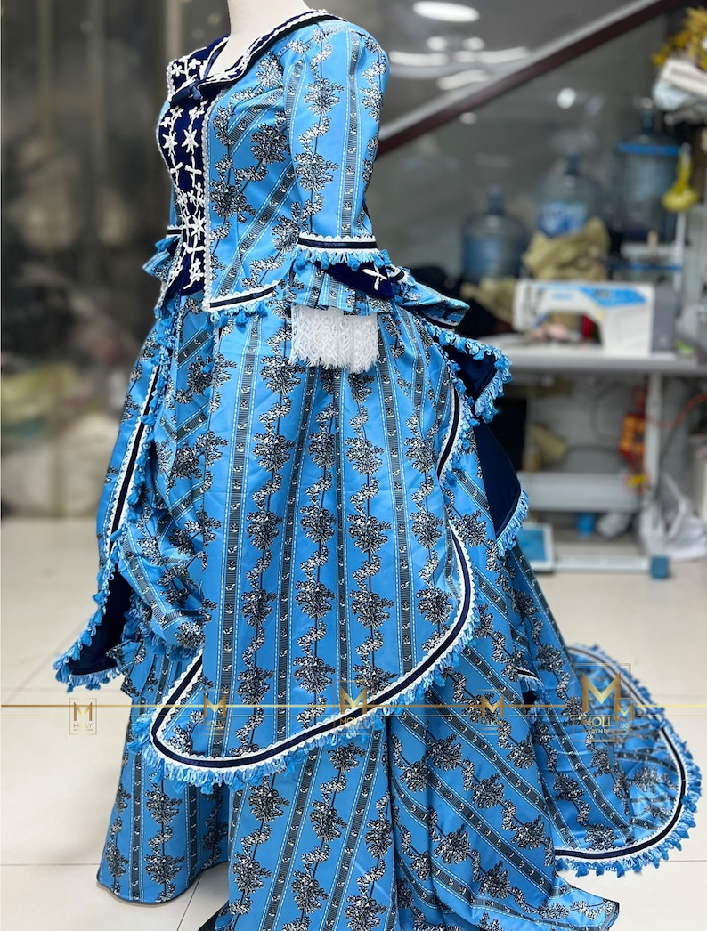 May include: A blue and white patterned dress with a ruffled skirt and a fitted bodice. The dress has a white lace trim and a blue velvet sash.