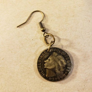 May include: A gold-toned earring featuring a coin with a profile of a woman's face. The coin has the text "DUITSCH INDIEN" around the edge.