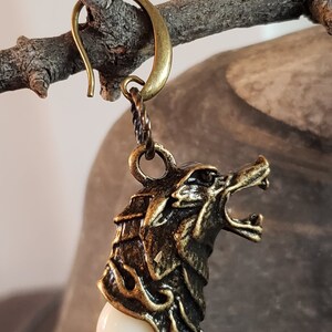 May include: A gold-toned wolf head earring with a white tooth charm. The earring has a hook closure.