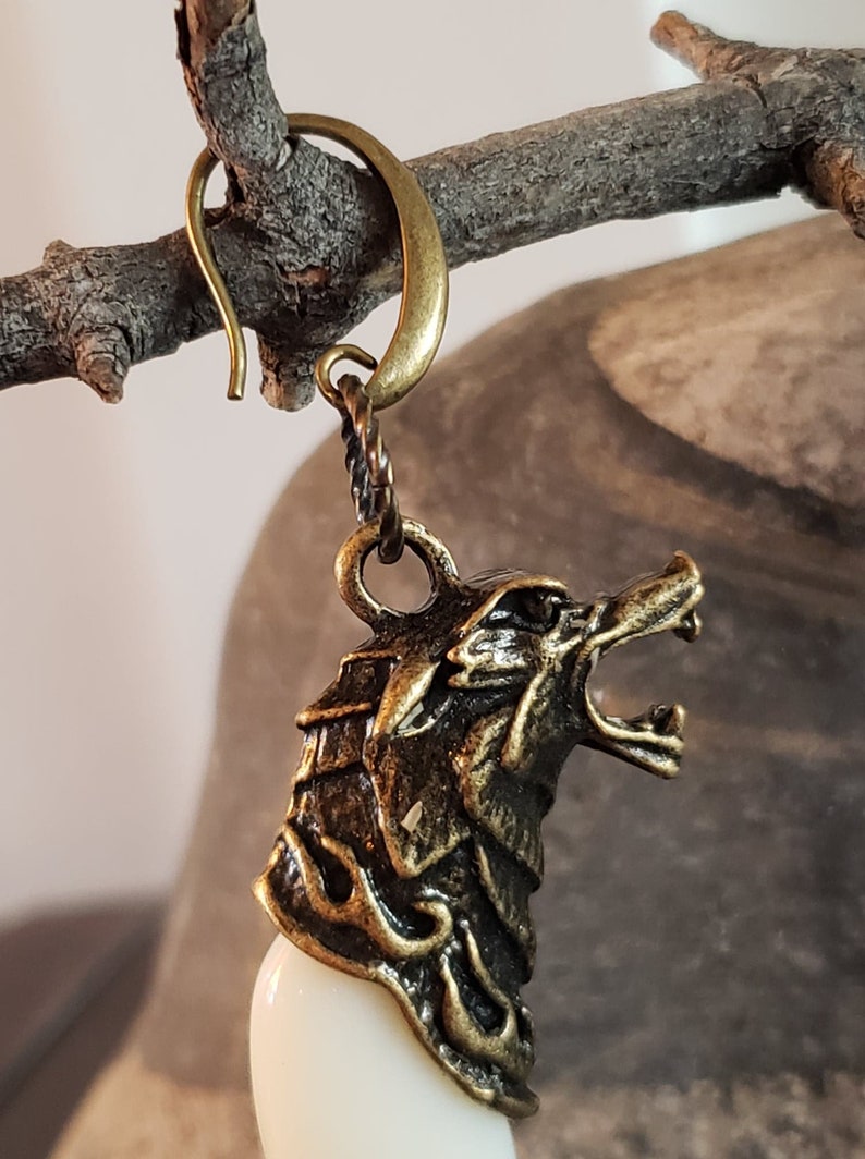 May include: A gold-toned wolf head earring with a white tooth charm. The earring has a hook closure.