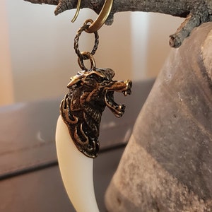 May include: A gold wolf head charm with a white fang pendant hanging from a gold hoop earring.