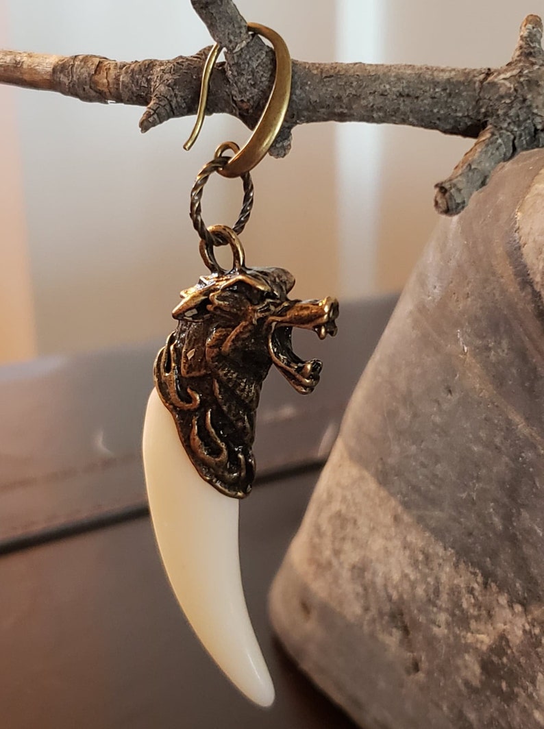 May include: A gold wolf head charm with a white fang pendant hanging from a gold hoop earring.