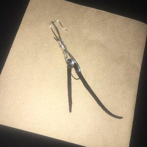May include: A silver wire earring with a black leather tassel hanging from it.