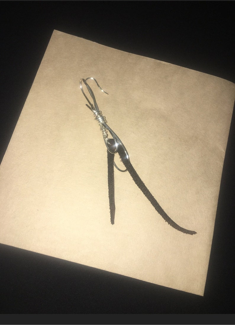 May include: A silver wire earring with a black leather tassel hanging from it.