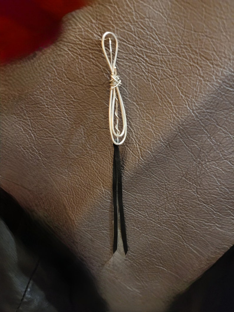 May include: A silver wire jewelry piece with a knotted design and black leather tassels.