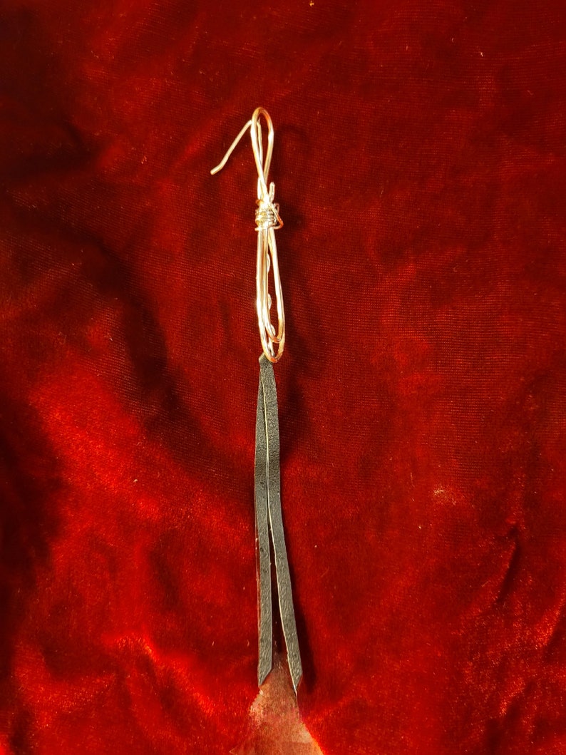 May include: A pair of long, black leather earrings with a silver wire knot at the top.