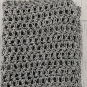K&ouml;nnte beinhalten: Nahaufnahme eines grau gestrickten Stoffes mit offenem Gewebe. Der Stoff hat ein strukturiertes Aussehen mit einem gitterartigen Muster aus offenen R&auml;umen. Das Garn scheint eine mittelgraue Farbe zu haben.