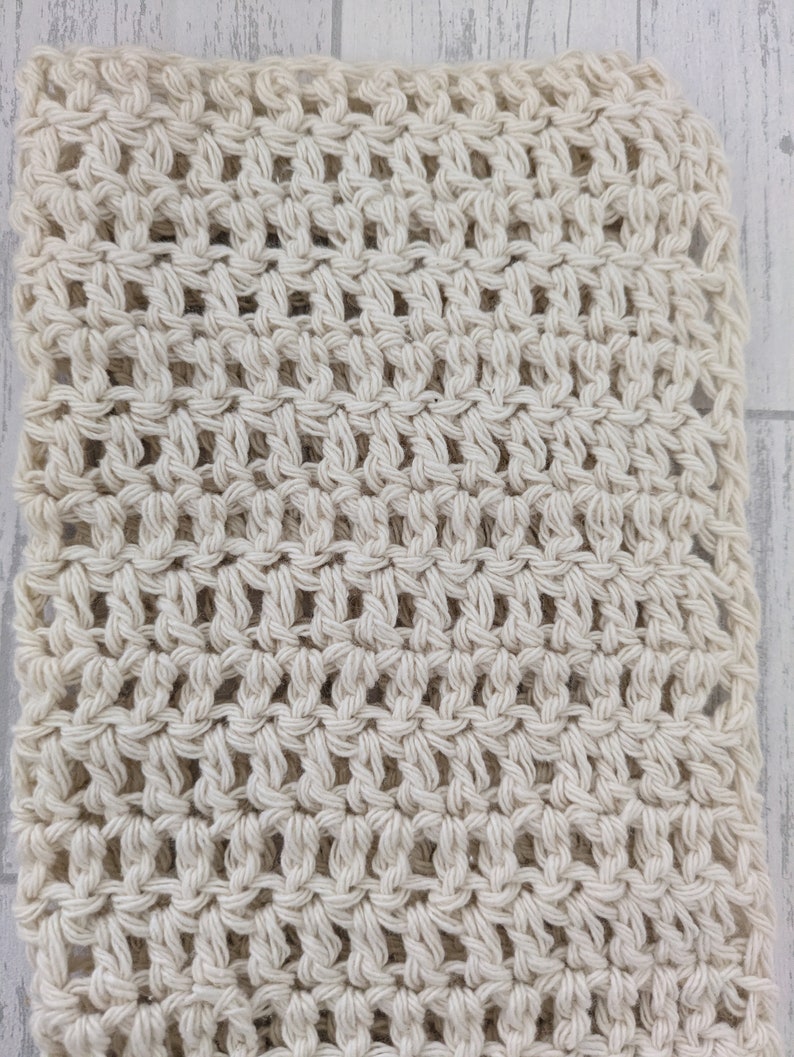 K&ouml;nnte beinhalten: Cremefarbener H&auml;kelstoff mit offenem Gewebe. Die Textur ist sichtbar, mit einem sich wiederholenden Muster aus Knoten und Zwischenr&auml;umen. Der Stoff wirkt weich und geschmeidig, geeignet f&uuml;r verschiedene Bastelprojekte oder Wohnaccessoires. Die neutrale Farbe macht ihn vielseitig.