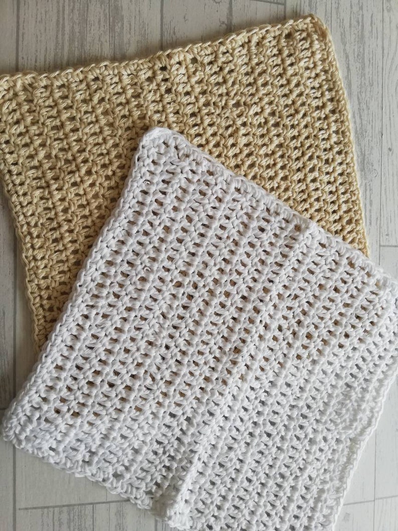 K&ouml;nnte beinhalten: Zwei geh&auml;kelte Waschlappen, einer in Creme und einer in Wei&szlig;, werden gezeigt. Die Waschlappen haben ein strukturiertes, offenes Webmuster. Der cremefarbene Waschlappen befindet sich hinter dem wei&szlig;en, der sich im Vordergrund befindet.