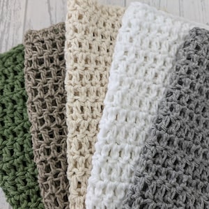 K&ouml;nnte beinhalten: Eine Sammlung von f&uuml;nf geh&auml;kelten Waschlappen in verschiedenen Farben: Gr&uuml;n, Braun, Beige, Wei&szlig; und Grau. Die Waschlappen sind nebeneinander angeordnet und zeigen ihr strukturiertes, offenes Webdesign. Die weichen, neutralen Farbt&ouml;ne erzeugen eine beruhigende &Auml;sthetik.