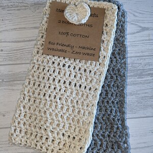 K&ouml;nnte beinhalten: Zwei handgefertigte Geschirrt&uuml;cher, eines cremefarbenes und eines graues, werden gezeigt. Das cremefarbene Tuch hat einen herzf&ouml;rmigen Knopf. Ein Etikett lautet "2 DISH CLOTHS, 100% COTTON, Eco Friendly - Machine Washable - Zero Waste."