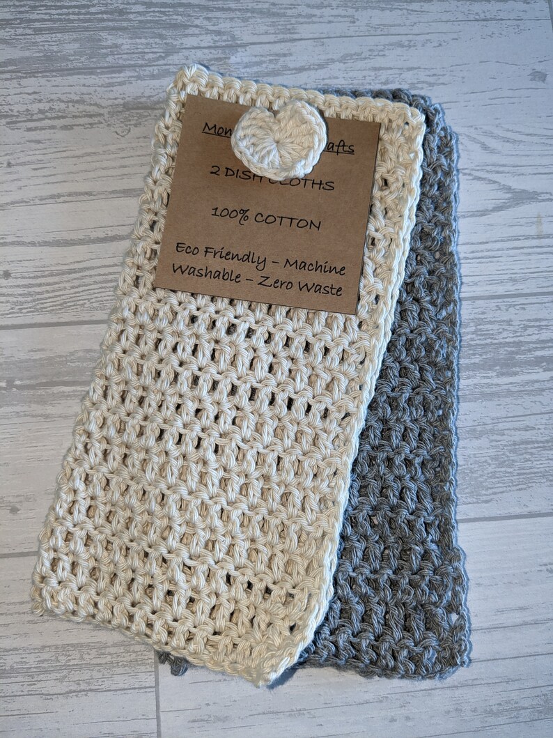 K&ouml;nnte beinhalten: Zwei handgefertigte Geschirrt&uuml;cher, eines cremefarbenes und eines graues, werden gezeigt. Das cremefarbene Tuch hat einen herzf&ouml;rmigen Knopf. Ein Etikett lautet "2 DISH CLOTHS, 100% COTTON, Eco Friendly - Machine Washable - Zero Waste."
