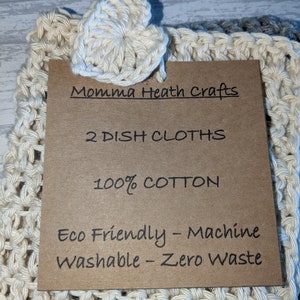K&ouml;nnte beinhalten: Zwei cremefarbene geh&auml;kelte Geschirrt&uuml;cher mit herzf&ouml;rmigem Akzent. Ein braunes Etikett lautet "Momma Heath Crafts", "2 DISH CLOTHS", "100% COTTON" und "Eco Friendly - Machine Washable - Zero Waste".