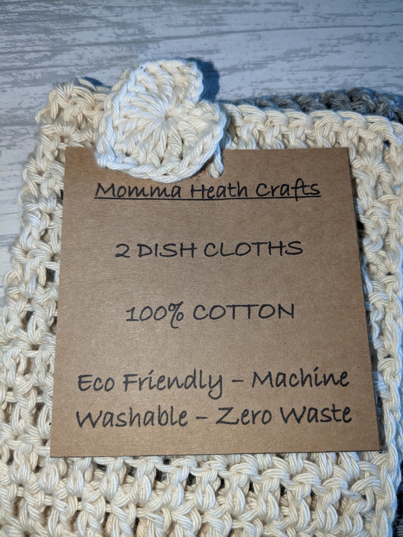 K&ouml;nnte beinhalten: Zwei cremefarbene geh&auml;kelte Geschirrt&uuml;cher mit herzf&ouml;rmigem Akzent. Ein braunes Etikett lautet "Momma Heath Crafts", "2 DISH CLOTHS", "100% COTTON" und "Eco Friendly - Machine Washable - Zero Waste".