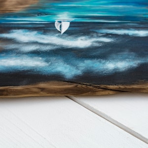 May include: A painting of a sailboat on a blue and white sea with white clouds. The painting is on a piece of wood with a natural edge.