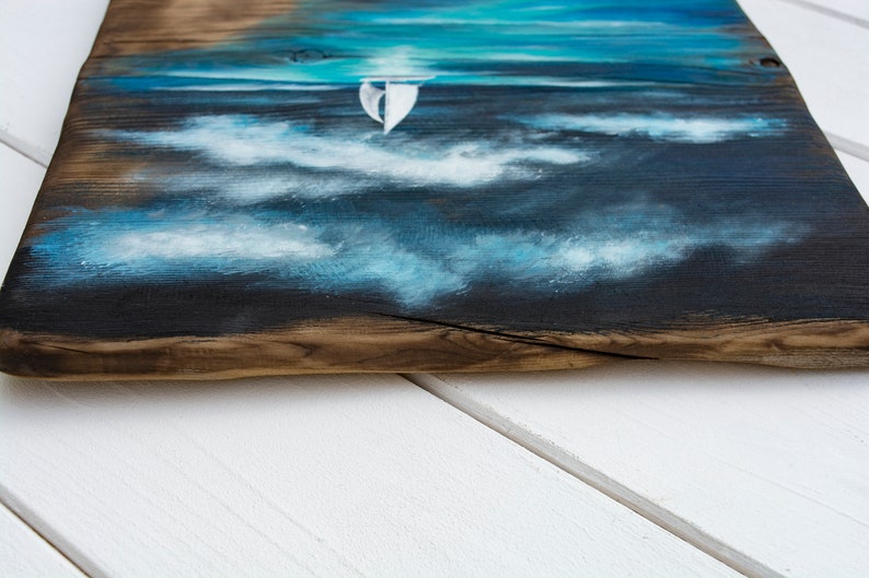 May include: A painting of a sailboat on a blue and white sea with white clouds. The painting is on a piece of wood with a natural edge.