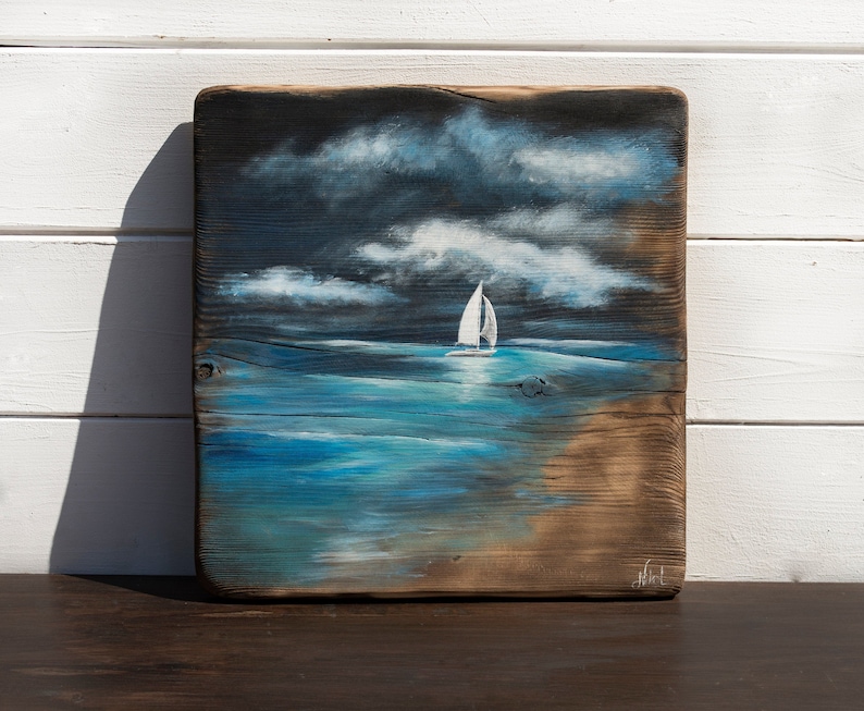 May include: A painting of a sailboat on a blue ocean with white clouds in the sky. The painting is on a piece of reclaimed wood.
