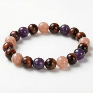 May include: A beaded bracelet featuring a variety of polished gemstones. The bracelet includes round beads in shades of brown, purple, and peach. The beads are strung together to form a circular shape, suitable for wrist wear.