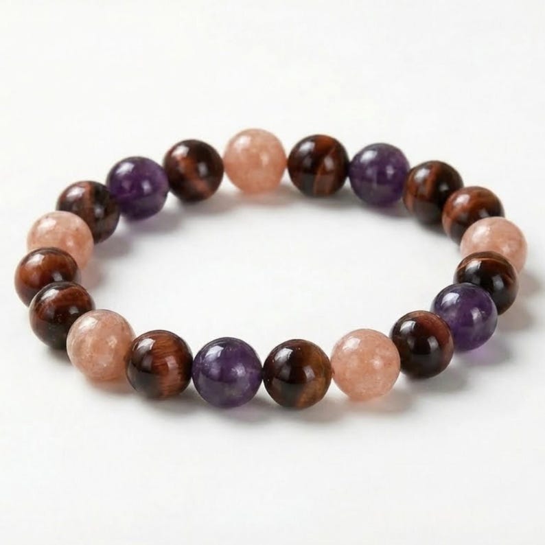 May include: A beaded bracelet featuring a variety of polished gemstones. The bracelet includes round beads in shades of brown, purple, and peach. The beads are strung together to form a circular shape, suitable for wrist wear.