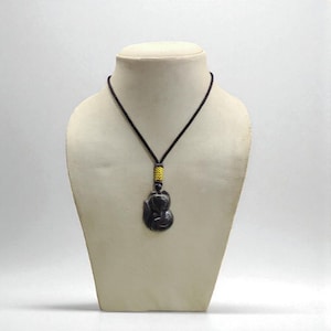 May include: A dark gray pendant necklace with a black cord. The pendant is a stylized figure, and the cord has a yellow and black accent. The necklace is displayed on a mannequin.